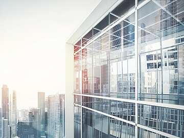 Modern glass office building with reflections of city skyscrapers in the windows, under a bright sky.