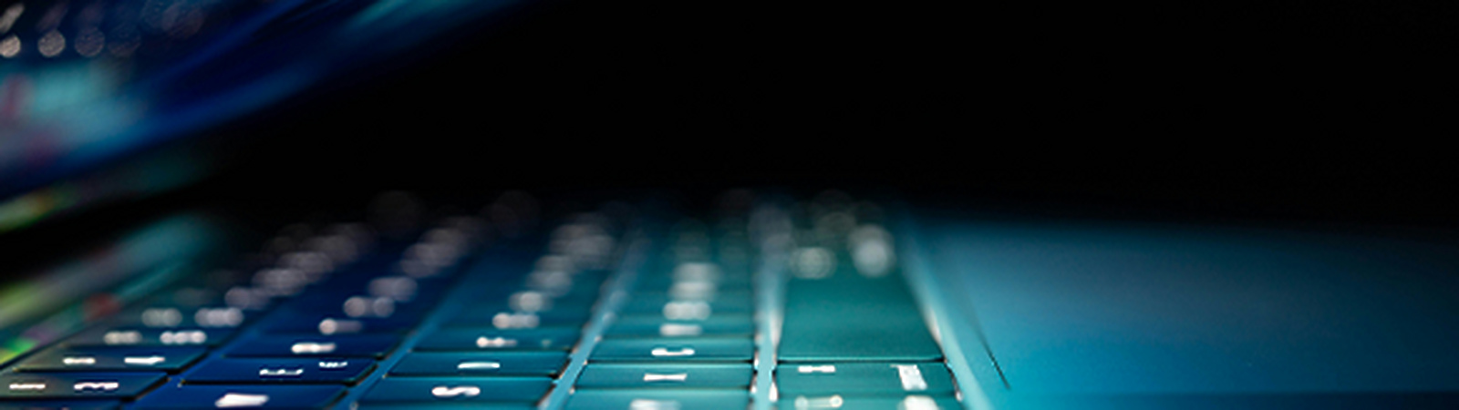 A close-up view of a laptop keyboard illuminated by soft blue light, with the screen partially closed, creating a sleek and futuristic atmosphere.