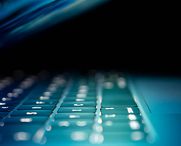 A close-up view of a laptop keyboard illuminated by soft blue light, with the screen partially closed, creating a sleek and futuristic atmosphere.
