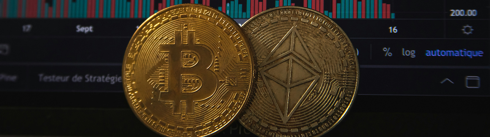 lose-up of physical Bitcoin and Ethereum coins placed in front of a computer screen displaying cryptocurrency price charts and trading data