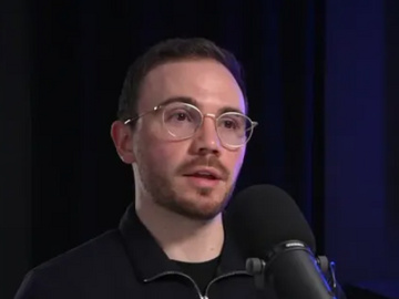 Person speaking into a microphone during a podcast recording in a studio setting.