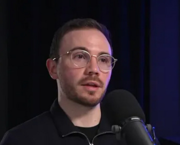 Person speaking into a microphone during a podcast recording in a studio setting.
