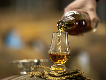 person pouring whiskey in an whiskey glass