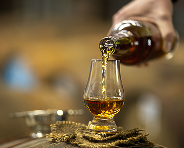 person pouring whiskey in an whiskey glass