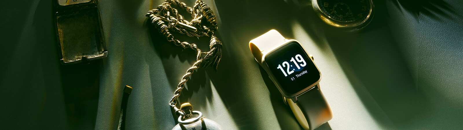 Different types of watches on a cloth with sunlight streaming over them. Examples with analog faces, a digital face, a pocket watch and a chain watch