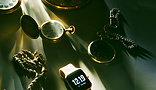 Different types of watches on a cloth with sunlight streaming over them. Examples with analog faces, a digital face, a pocket watch and a chain watch