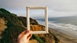 An empty picture frame held up in front of cliffs, beach and sea