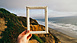 An empty picture frame held up in front of cliffs, beach and sea