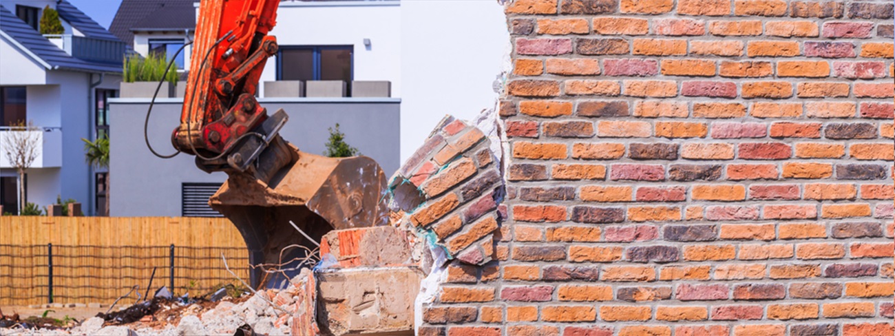 Destroyed brick wall and excavator. The demolition of the old house on the new white house background