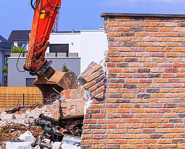 Destroyed brick wall and excavator. The demolition of the old house on the new white house background