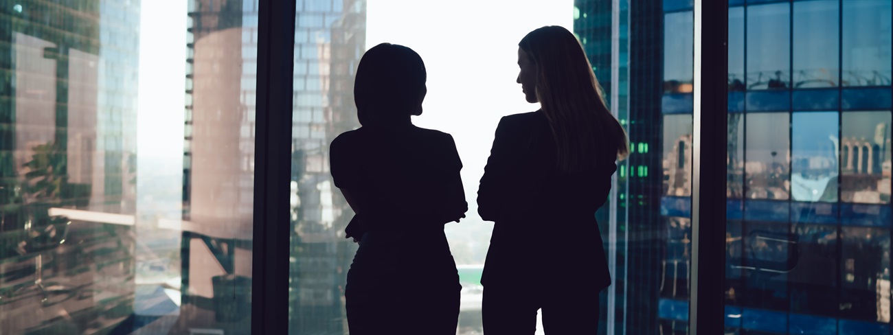 Two women talking in front of window