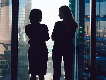 Two women talking in front of window