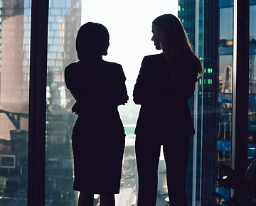 Two women talking in front of window