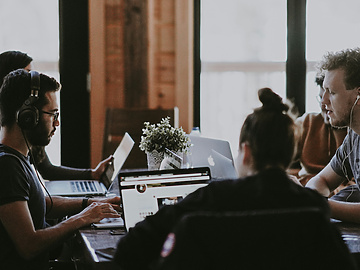 a group of people sitting around a table with laptops
