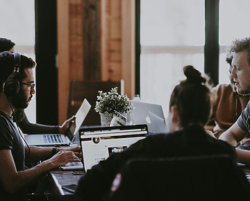 a group of people sitting around a table with laptops