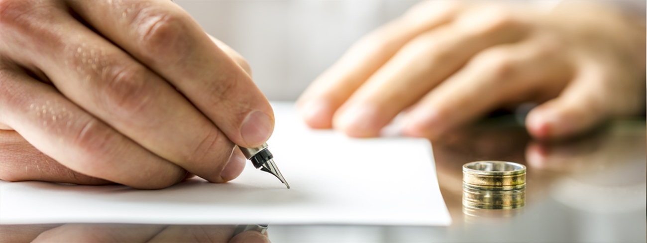 Man signing divorce papers with wedding ring on the table