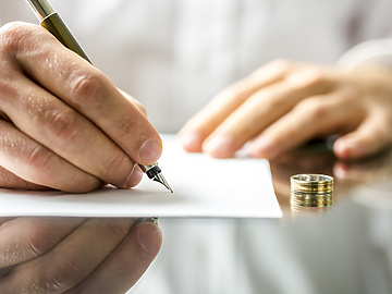 Man signing divorce papers with wedding ring on the table