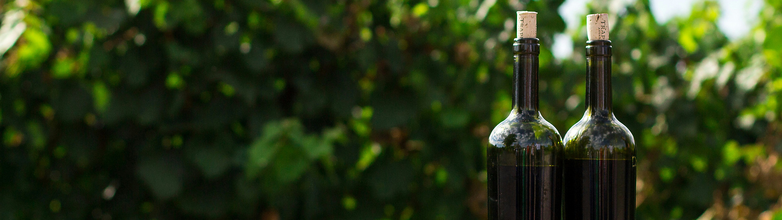 two black glass bottles on the top of the brown wooden barrel