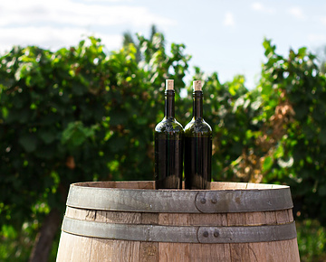 two black glass bottles on the top of the brown wooden barrel