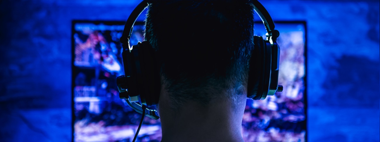 Male with headphones playing online video game on computer