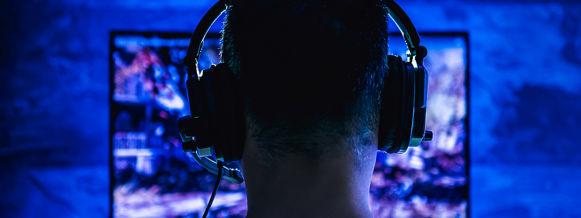 Male with headphones playing online video game on computer
