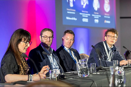 People seated at a panel discussion with microphones at a conference event.