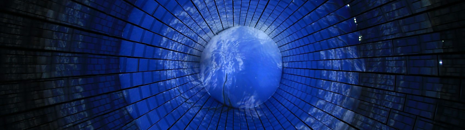 A circular, tunnel-like structure with a glowing blue center resembling Earth, surrounded by dark, radial grid patterns that create a sense of depth and perspective.