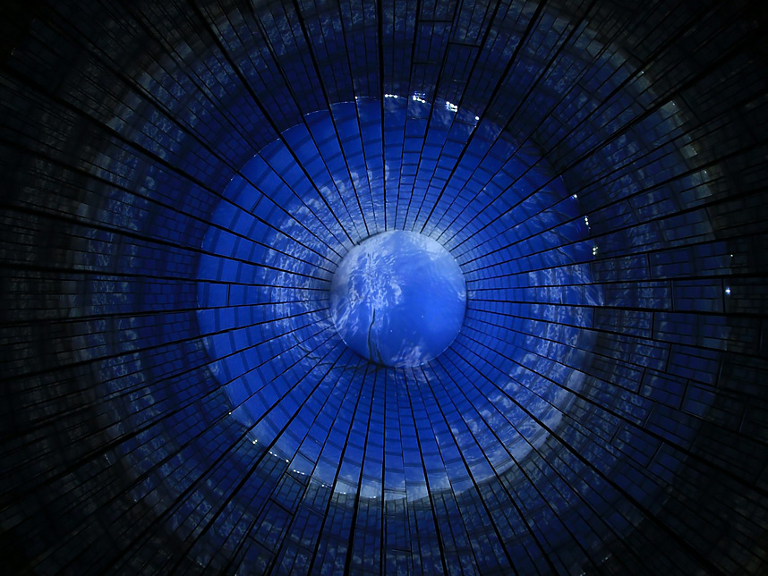 A circular, tunnel-like structure with a glowing blue center resembling Earth, surrounded by dark, radial grid patterns that create a sense of depth and perspective.