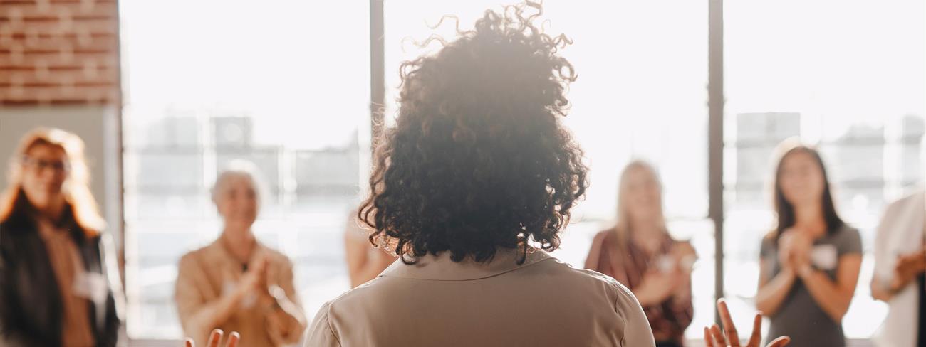 Woman giving a speech in front of a group of women.