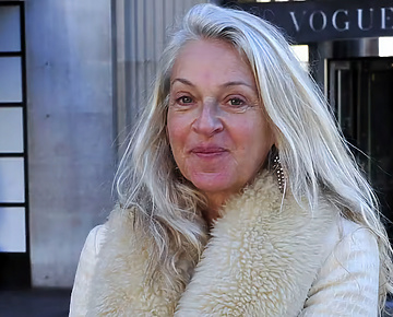 Sue Douglas, British media executive and former newspaper editor, wearing a white coat, pictured outside. In view a partially obscured sign in the background displaying the word Vogue