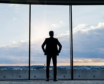 A man looking out of a glass building over a city