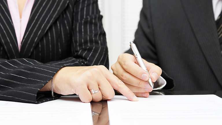a close-up of a person and a person signing papers
