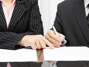a close-up of a person and a person signing papers