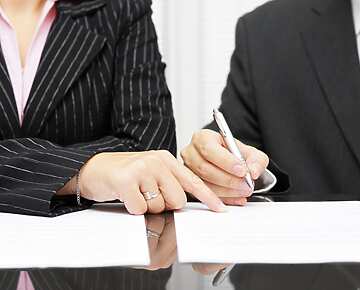 a close-up of a person and a person signing papers