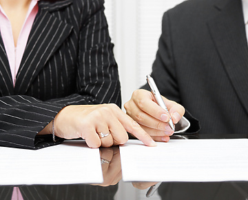 a close-up of a person and a person signing papers