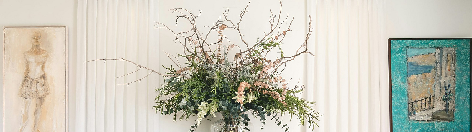 A decorative interior scene featuring a wooden console table with ornate carvings, topped with a large floral arrangement in a glass vase.