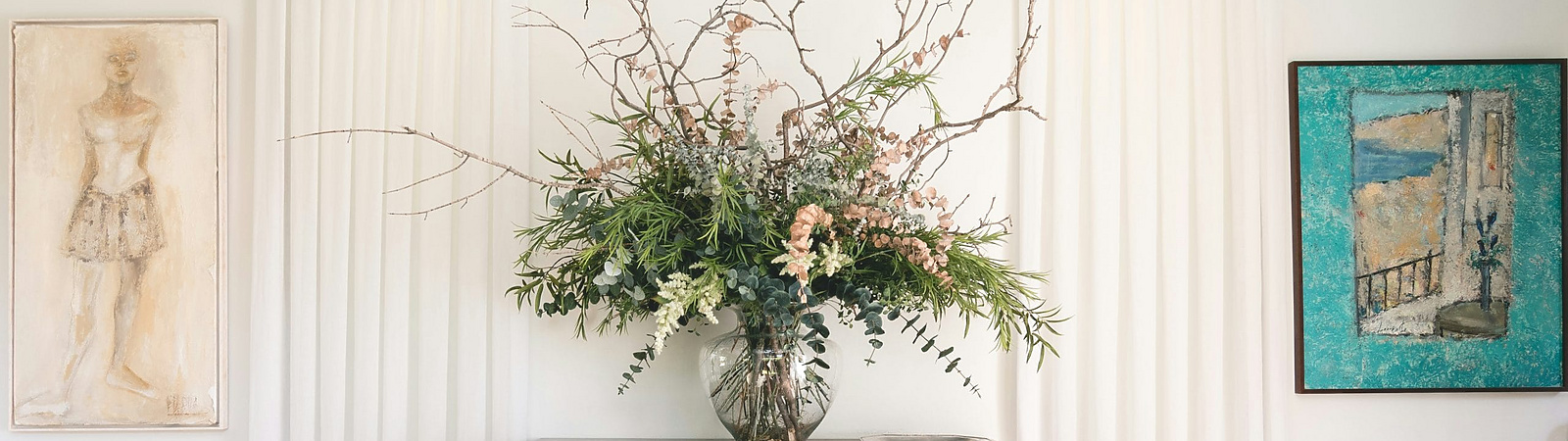 A decorative interior scene featuring a wooden console table with ornate carvings, topped with a large floral arrangement in a glass vase.