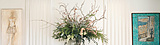 A decorative interior scene featuring a wooden console table with ornate carvings, topped with a large floral arrangement in a glass vase.