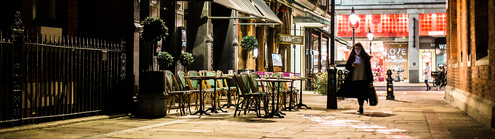 a person walking on a sidewalk with chairs and a lamp post