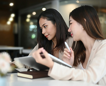 2 women at a desk in an office looking at paperwork and a laptop