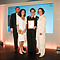 Four people stand together on stage at an awards event. One woman in the center is holding a framed certificate.