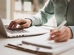 person typing on laptop and writing