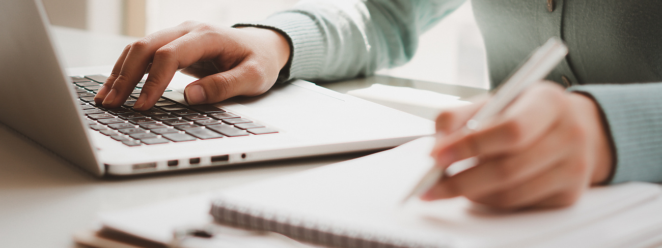 person typing on laptop and writing
