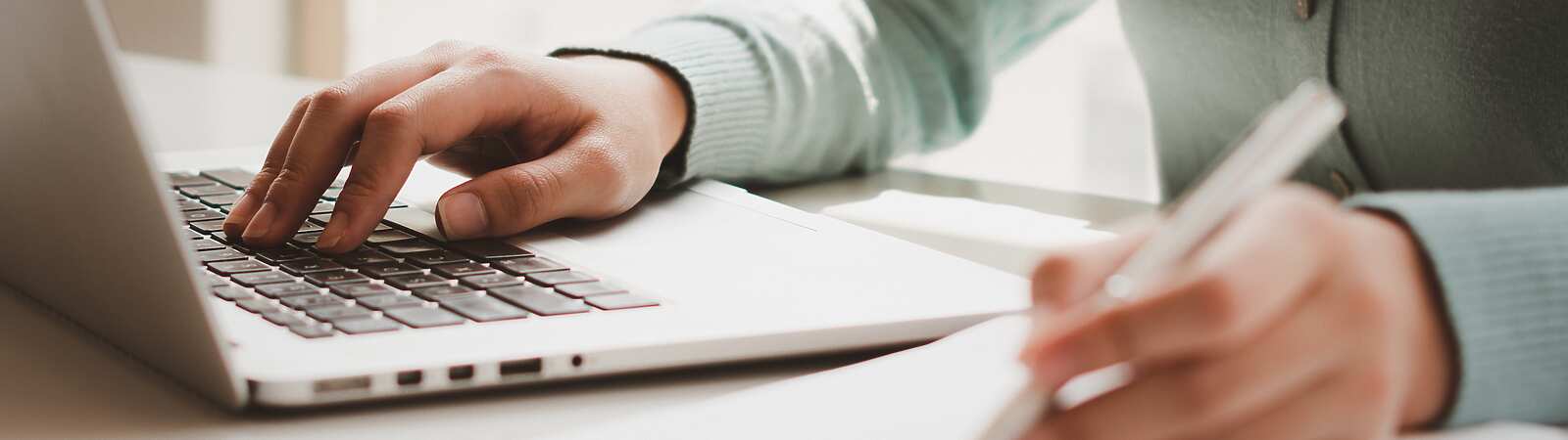 person typing on laptop and writing