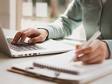 person typing on laptop and writing
