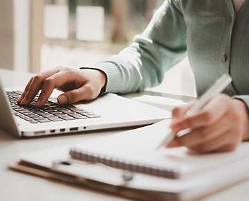 person typing on laptop and writing