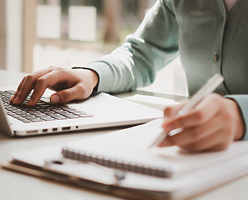 person typing on laptop and writing