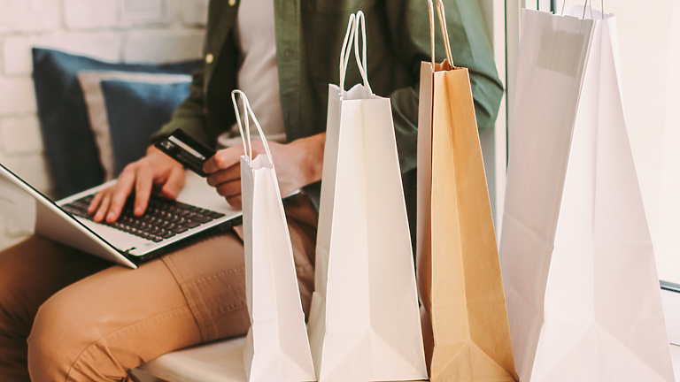 Man working on laptop with four retails bags next to him