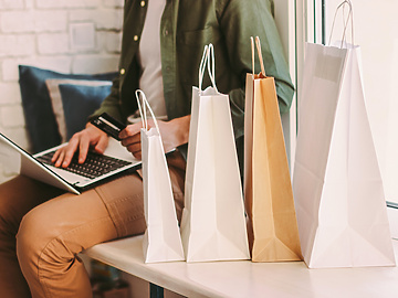 Man working on laptop with four retails bags next to him