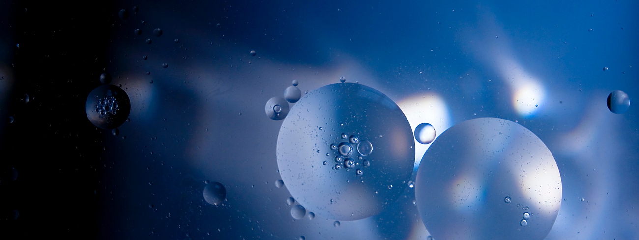 Abstract image of translucent oil droplets suspended in blue liquid, illuminated by light reflections and shadows, creating a soft, ethereal effect.